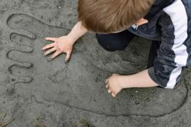 Gutt som sitter på kne og ser på et kjempestort fotspor i sanden