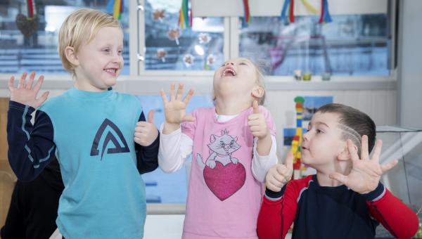 Tre barn som ler og har thumbs up