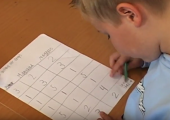 Gutt i blå genser som løser matematikkoppgave i tabell på et ark. 